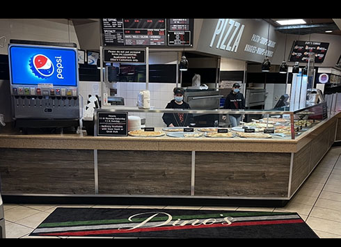 Inside Dino's Pizza and Restaurant showing the counter and kitchen where fresh pizza is made daily